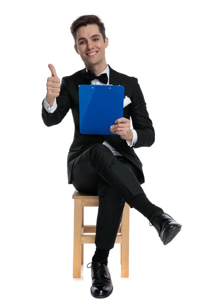 Счастливый молодой элегантный мужчина, держащий буфер обмена и делающий большие пальцы вверх s — стоковое фото