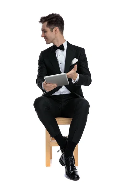 Young elegant man in tuxedo holding tab and looking to side — 스톡 사진