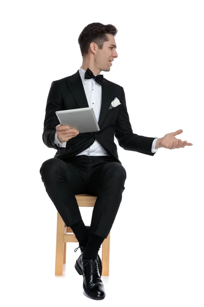 Elegant modern man in tuxedo holding tab and chatting — Stock Photo, Image