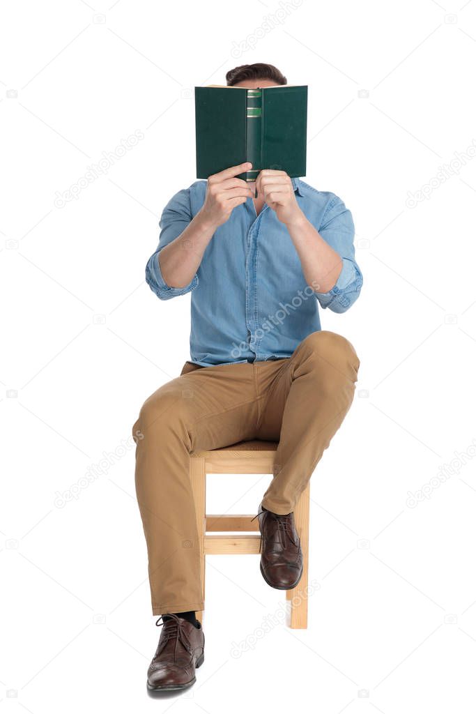 young casual man hiding behind book and sitting