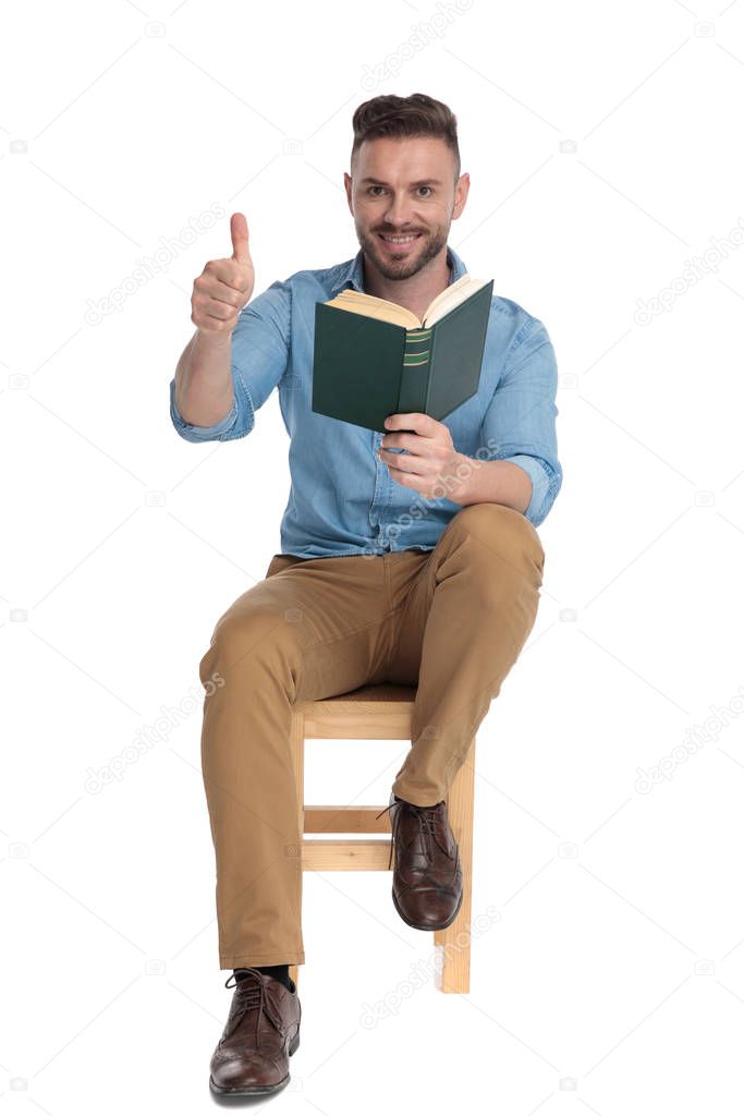 young casual man holding book and making thumbs up sign