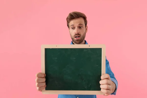 Chocado casual cara segurando vazio blackboard — Fotografia de Stock