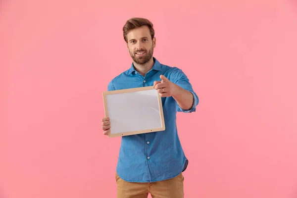 Happy casual guy holding empty board and pointing finger — Stock Photo, Image