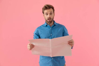 Gazete okuyan, kot gömlekli, şaşkın bir adam.