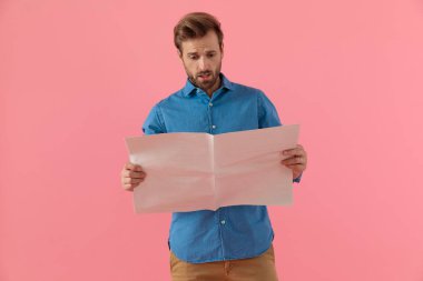 Gazete okuyan kot gömlekli genç adam şok oldu.