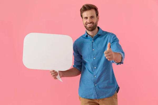 Sonriente joven chico sosteniendo el habla burbuja y haciendo pulgares arriba sig —  Fotos de Stock