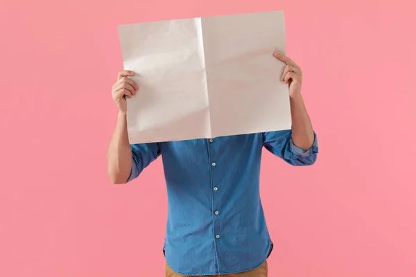 新聞で顔を覆うデニムシャツのカジュアルな男 — ストック写真