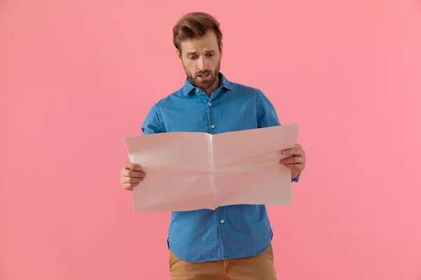 shocked young guy in denim shirt reading newspaper