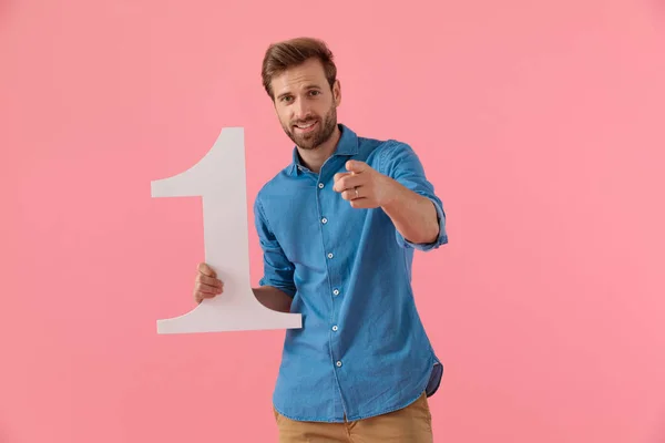 Happy casual guy holding number one sign and pointing finger — Stock Photo, Image