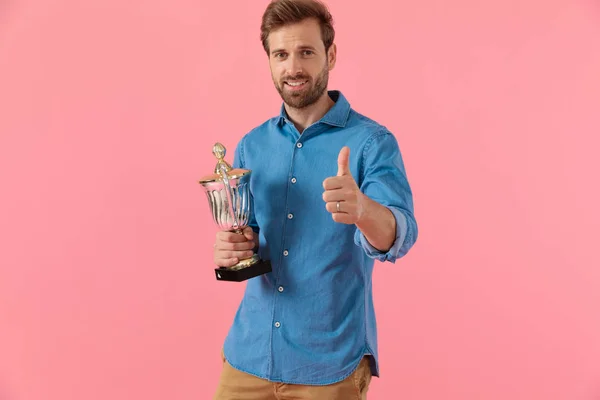 Happy casual guy holding trophy and making thumbs up sign — Stock Photo, Image