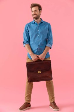 happy young guy in denim shirt smiling and holding suitcase