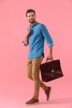 happy casual man holding suitcase and fixing shirt