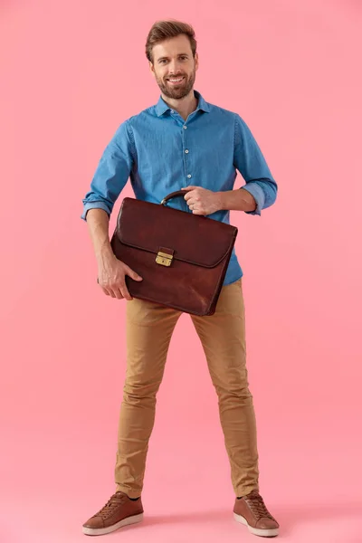 Gelukkig casual guy in denim shirt glimlachen en houden koffer — Stockfoto