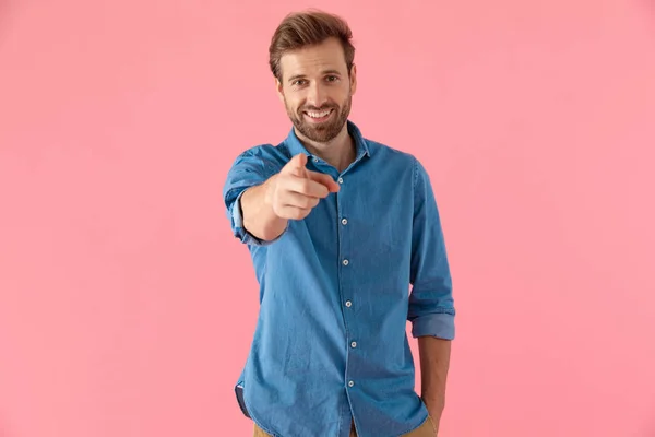 Счастливый случайный человек в джинсовой рубашке улыбаясь и указывая пальцем — стоковое фото