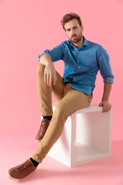 Hombre casual serio en camisa de mezclilla sosteniendo el codo en la rodilla —  Fotos de Stock
