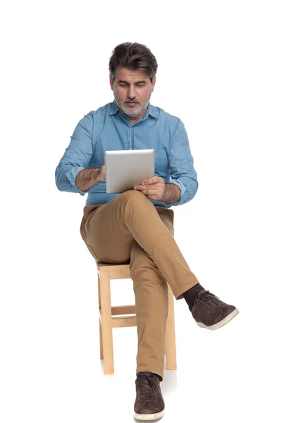 Entspannter Gelegenheitsmensch beim Lesen und Schreiben auf seinem Tablet — Stockfoto