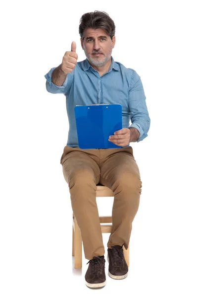 Positieve casual man houdt een klembord en het geven van duimen omhoog — Stockfoto