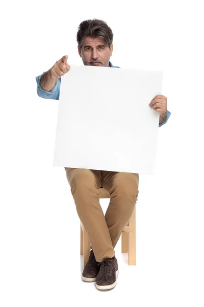 Zelfverzekerde toevallige man die een leeg reclamebord vasthoudt en naar voren wijst — Stockfoto