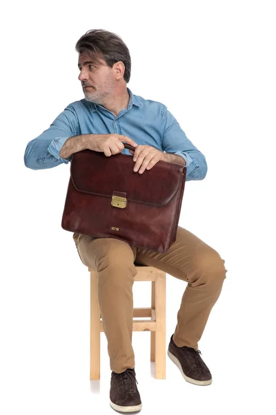 Сосредоточенный случайный человек смотрит в сторону и держит свой портфель — стоковое фото