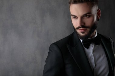 sexy businessman wearing black tuxedo and looking away pensive 