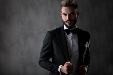 İş adamı kameraya bakarken dikiliyor ve ceketi tamir ediyor