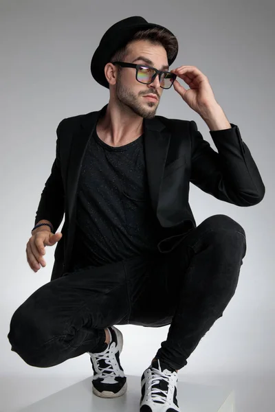 Cool young man fixing glasses and crouching — Stock Photo, Image