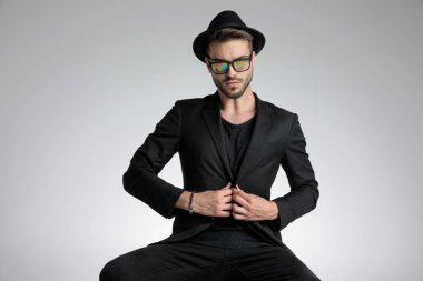 sexy cool guy arranging coat and sitting in a fashion pose