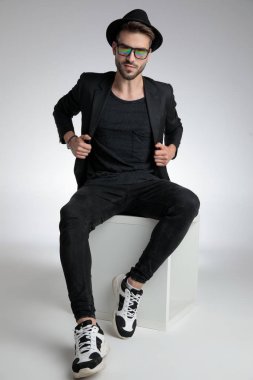 sexy cool guy pulling coat and sitting on grey background