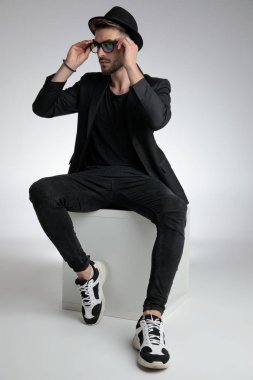 cool young man looking to side and fixing sunglasses