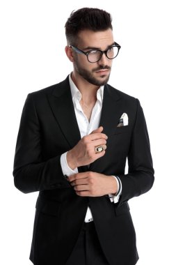 businessman standing and fixing sleeve while looking away pensiv