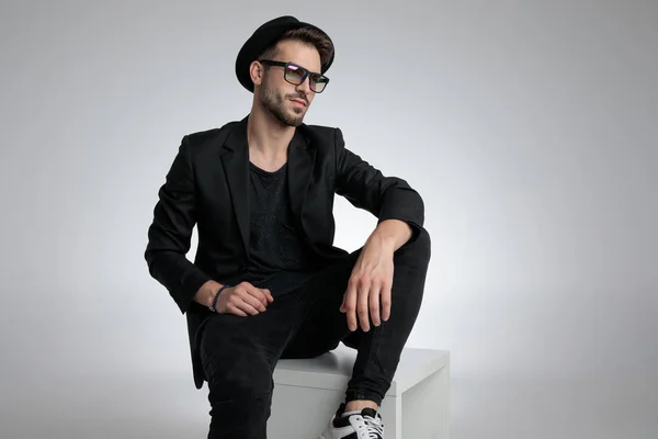 Cool fashion guy looking to side and sitting in a fashion pose — Stockfoto