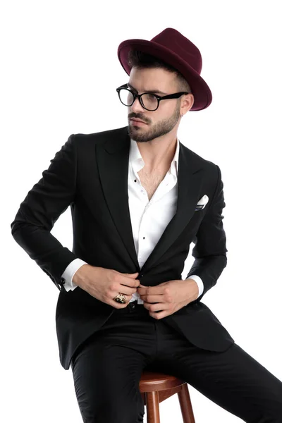 Бизнесмен в бордовой шляпе сидит и чинит куртку — стоковое фото