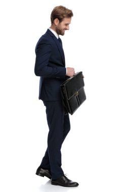 Mavi takım elbiseli mutlu bir işadamı elinde bavul ve gülümsüyor.