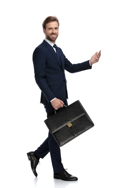 Щасливий бізнесмен посміхається, тримає валізу і презентує — стокове фото