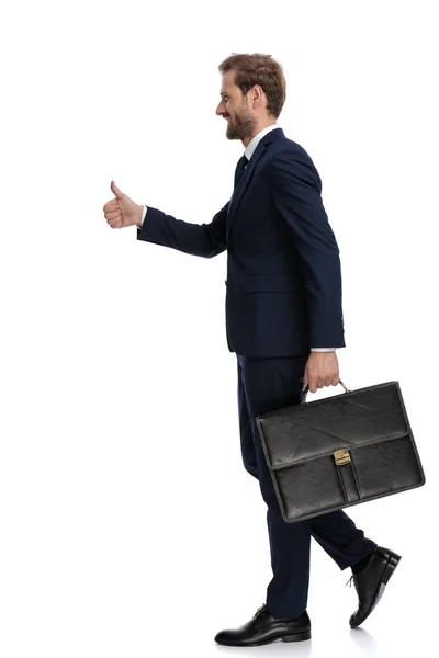 Jovem empresário feliz segurando mala e fazendo polegares até si — Fotografia de Stock