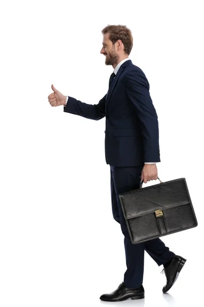 Feliz joven empresario sosteniendo la maleta y haciendo pulgares hacia arriba si — Foto de Stock