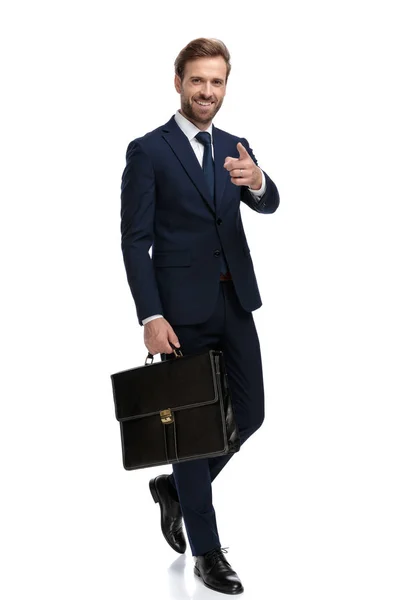 Szczęśliwy biznesmen trzymając walizkę i wskazując palcem — Zdjęcie stockowe