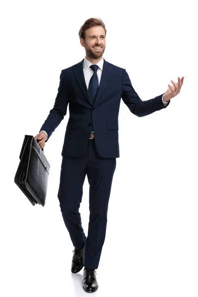 Happy young businessman holding suitcase and presenting to side — Stock Photo, Image