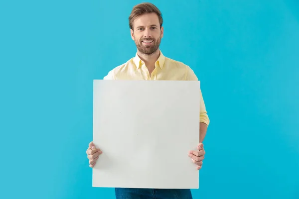 Cheerful casual man smiling and holding a blank billboard — 图库照片