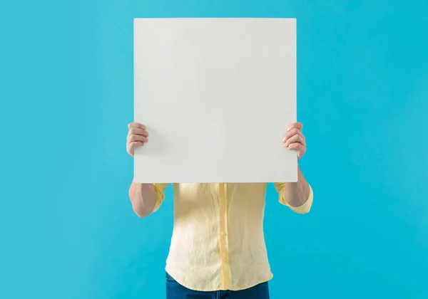 Young casual man hiding his face behind a blank billboard — Stockfoto