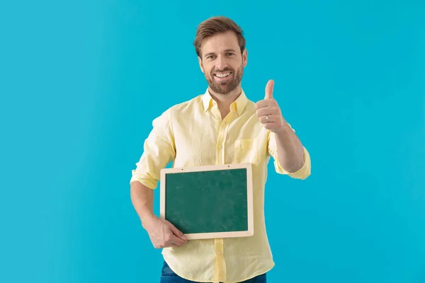 Casual man giving a thumbs up and holding a blackboard — Stockfoto