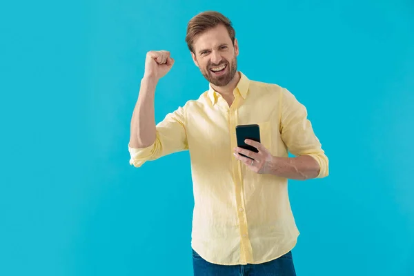 Boldog alkalmi férfi nevet és ünnepel, kezében egy telefon — Stock Fotó