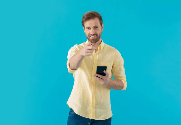 Confident casual man pointing forward and holding a phone — 图库照片