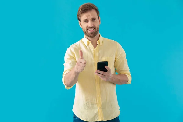 Casual man giving a thumbs up and holding his phone — ストック写真