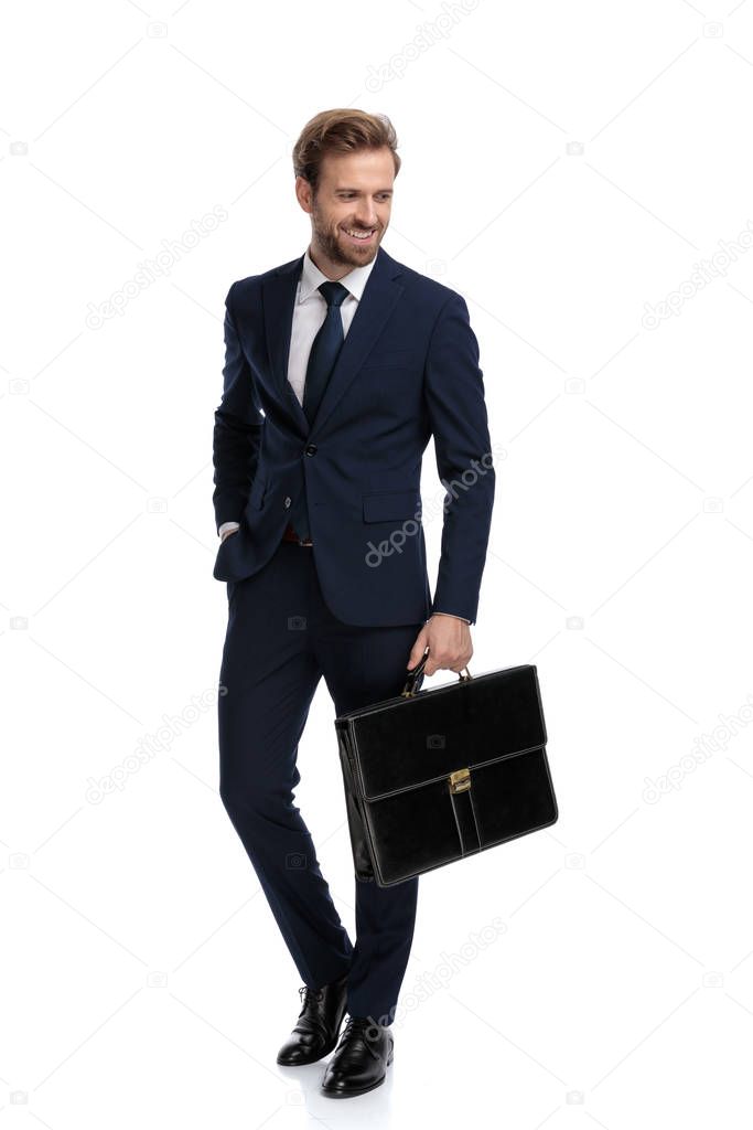 smiling young businessman in navy blue suit holding suitcase