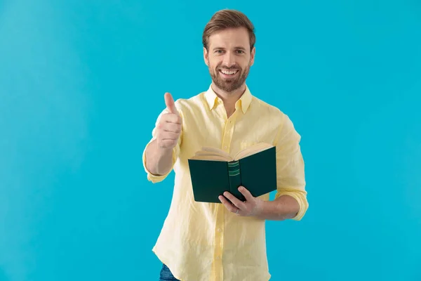 Lässiger Mann, der den Daumen hebt und ein Buch in der Hand hält — Stockfoto