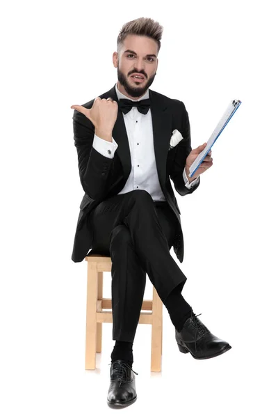 Businessman sitting and holding clipboard while pointing aside d — Stok fotoğraf