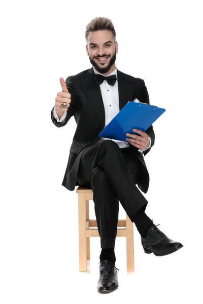 Hombre de negocios sentado y sujetando el portapapeles mientras da pulgares hacia arriba — Foto de Stock