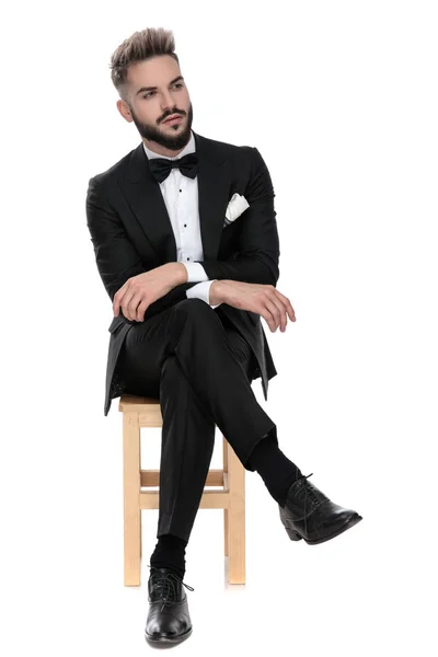 Uomo d'affari seduto con le braccia e le gambe piegate mentre distoglie lo sguardo — Foto Stock