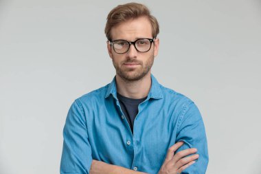 Kendine güvenen genç adam kollarını kavuşturup gülümsüyor.